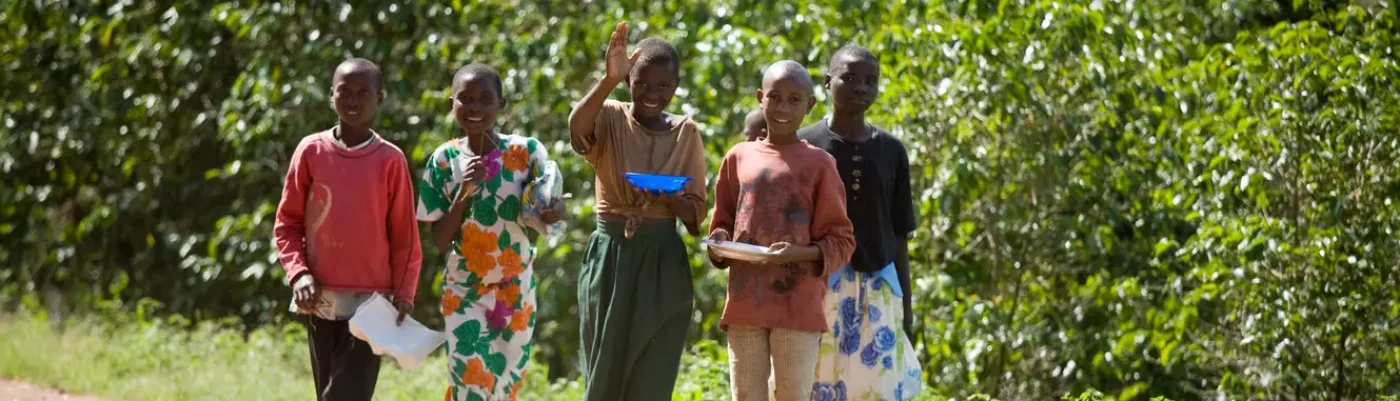 Group of African children walking together on a rural path surrounded by greenery.